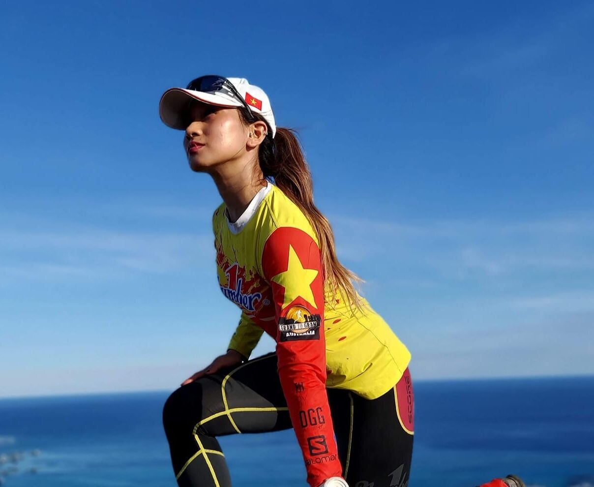Vũ Phương Thanh trong trang phục chạy bộ cờ đỏ sao vàng, quỳ trên mỏm đá bên biển
