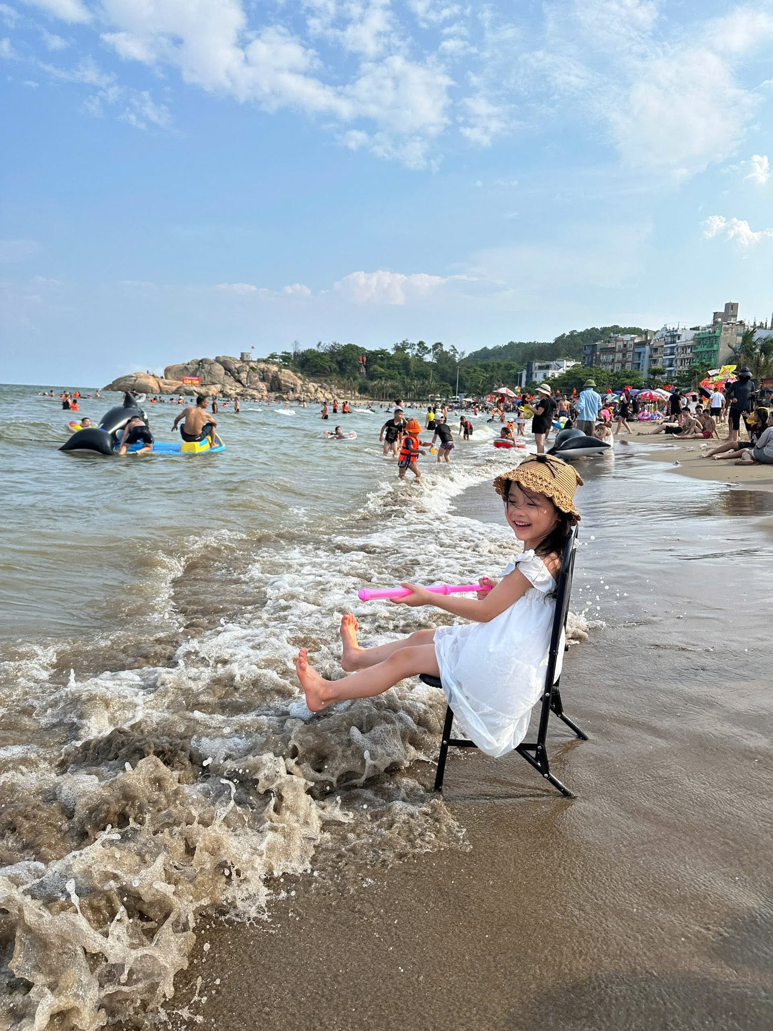 Một bé gái ngồi trên ghế cười đùa khi sóng biển vỗ vào chân trên bãi biển Sầm Sơn