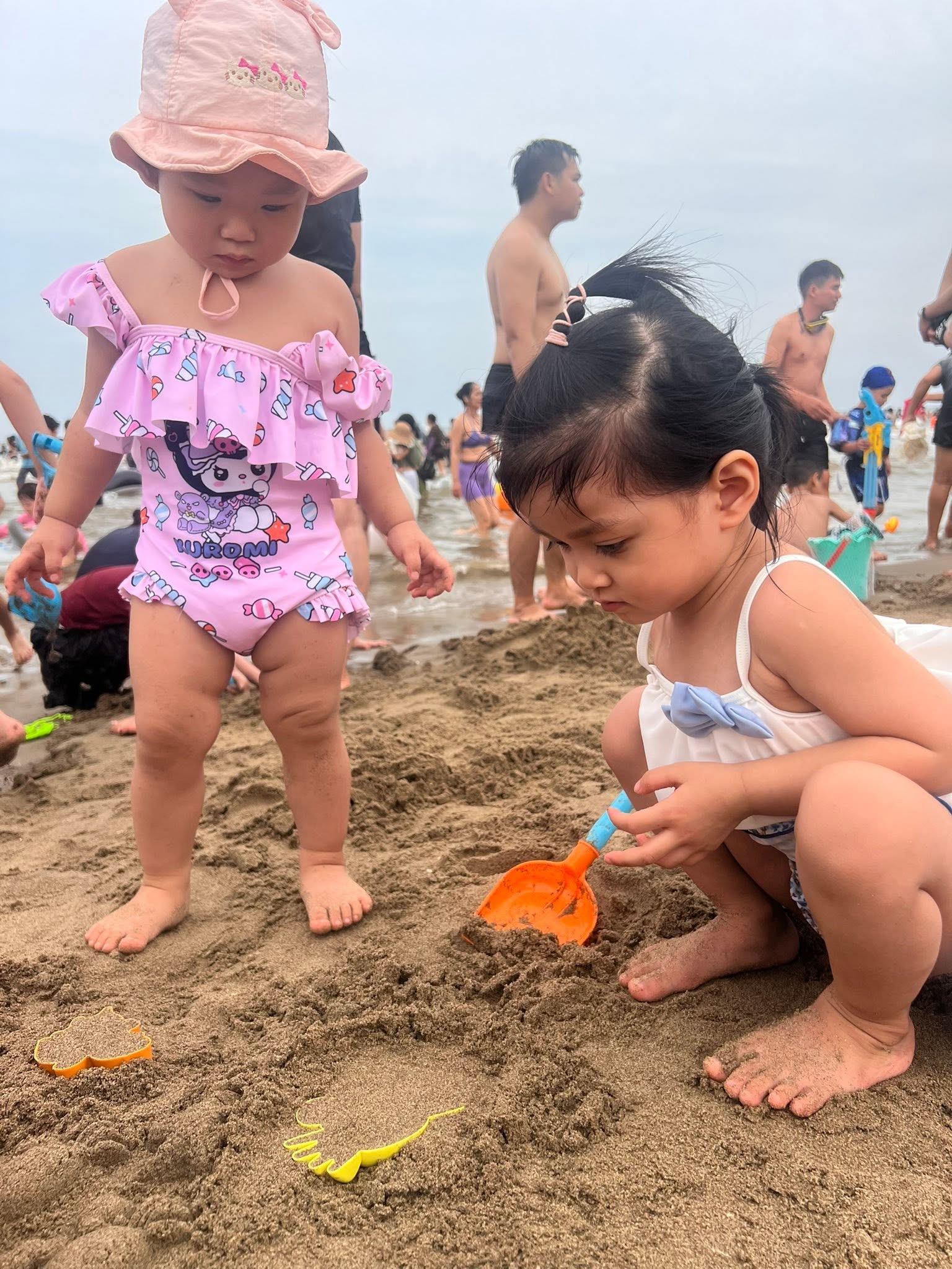 Hai bé gái chơi đùa với xô cát trên bãi biển
