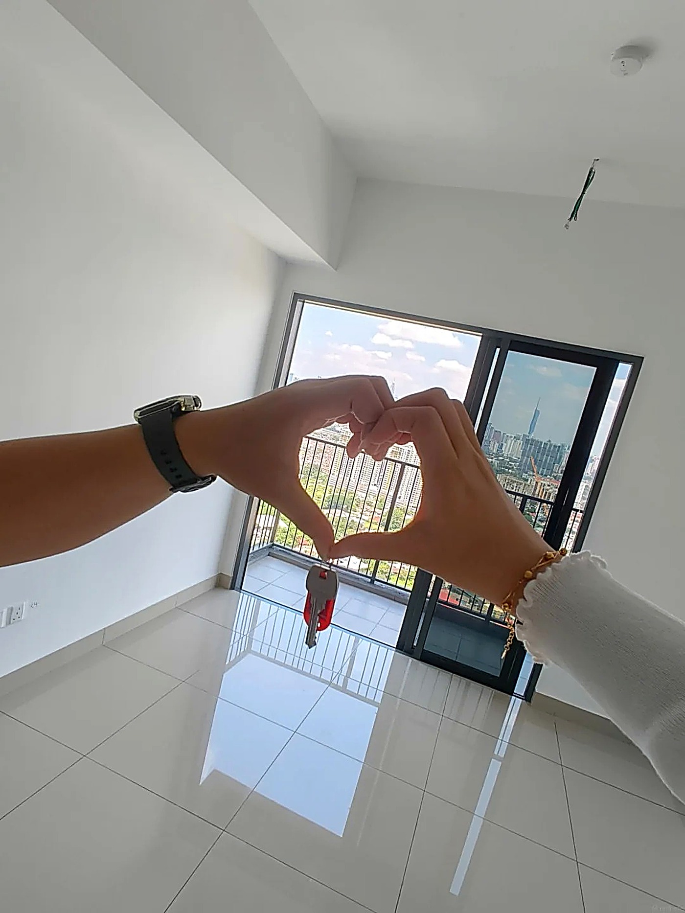 Hai người tạo hình trái tim bằng tay, giữ chìa khóa nhà mới, phía sau là view thành phố